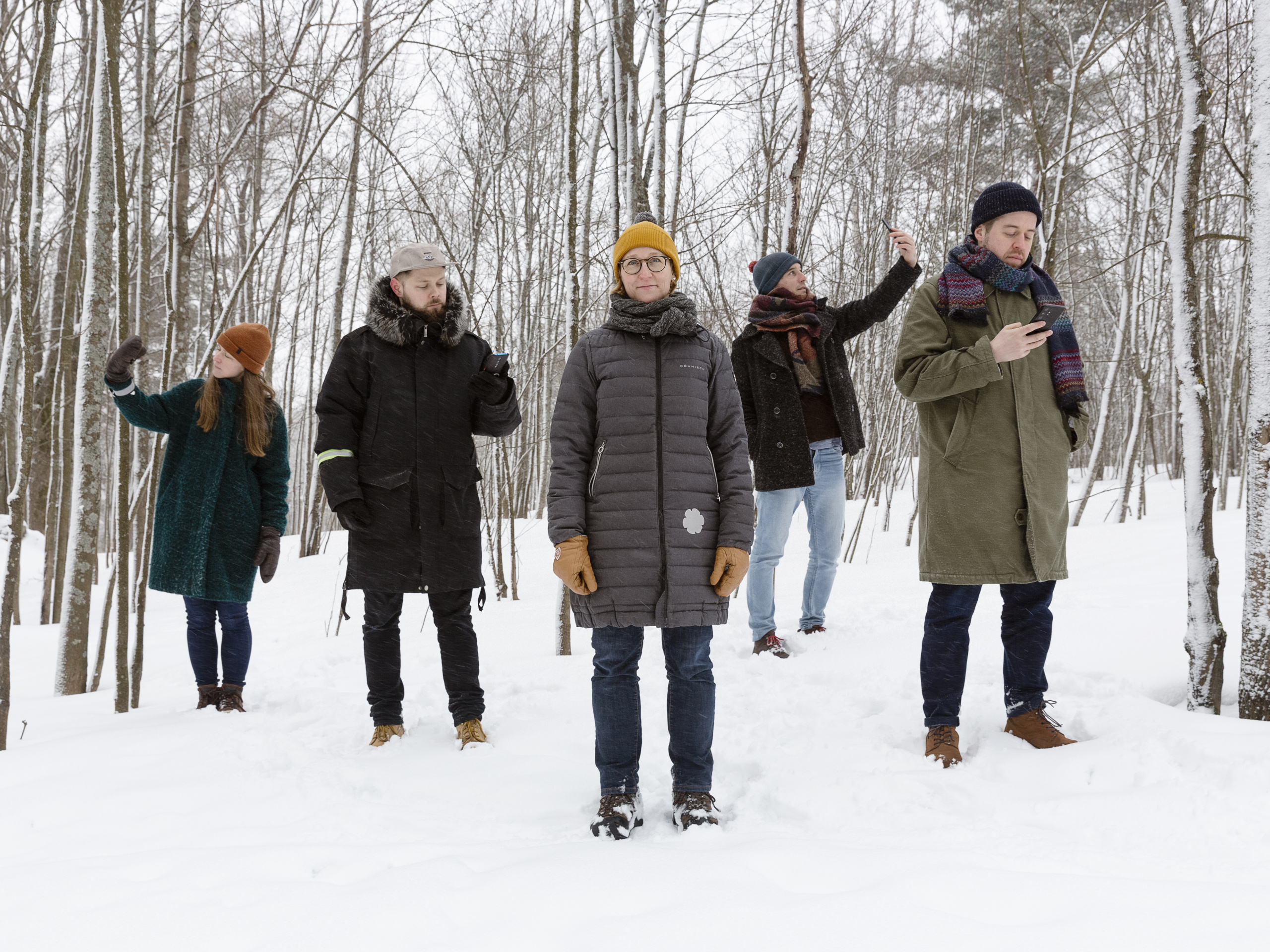 Kuvassa tutkijat seisovat lumisessa metsässä puhelimet käsissään.