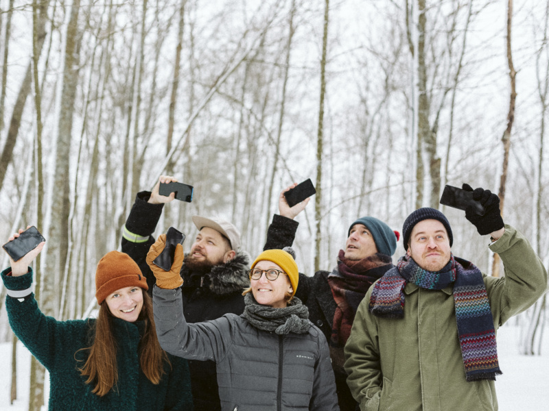Tutkijat seisovat lumisessa metsässä ja nostavat ylös käsissään pitämänsä puhelimet.